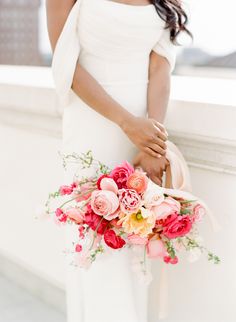 a woman holding a bouquet of flowers in her hand while standing next to a wall