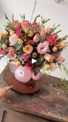 a vase filled with pink and yellow flowers on top of a wooden table in front of a white wall