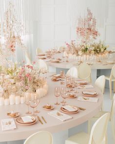 the table is set with white chairs and pink flowers in vases, gold place settings