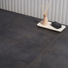 a black tile floor with a vase and sticks on it next to a soap dish