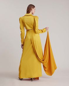 Exude luxury in the timeless silhouette of the DANCING gown. This floor length gown is made from a silky faux wrap fabric, in a soft golden yellow hue with buttons detailing on the torso, creating a waterfall gathering which moves across the body of the gown. Enhanced with a menswear inspired collar, this floor length gown is finished with french cuffs which allow for interchangeable cufflinks. The lower back features a peek a boo cutout and half train with a finger loop for a beautiful touch of Pre-draped Long Sleeve Wedding Gown, Wedding Dresses With Set-in Long Sleeves, Formal Satin Floor-length Sets, Formal Floor-length Satin Sets, Pre-draped Floor-length Evening Sets, Formal Fitted Maxi Length Sets, Formal Fitted Maxi Sets, Fitted Satin Floor-length Set, Fitted Floor-length Satin Set