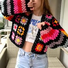 a woman standing in front of a window wearing a crocheted jacket and jeans