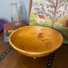 a wooden bowl sitting on top of a table next to books and a glass vase