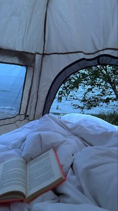 an open book sitting on top of a bed under a tent next to the ocean