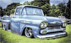 an old blue truck parked on top of a lush green field next to other cars