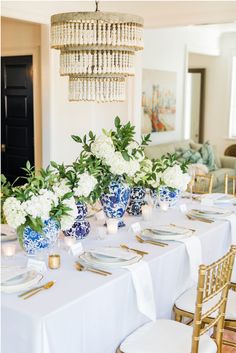 the table is set with blue and white dishes, gold place settings, and greenery