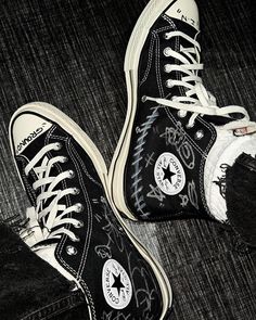 black and white shoes with graffiti on them sitting on the floor in front of a pair of jeans