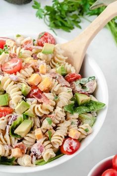 a white bowl filled with pasta salad next to tomatoes and avocado on the side