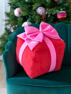 a red present wrapped in pink ribbon sitting on top of a green chair next to a christmas tree