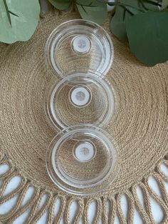 three clear glass bowls sitting on top of a woven table cloth next to green leaves