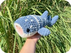 a hand holding a small blue and white crocheted stuffed animal in front of some tall grass