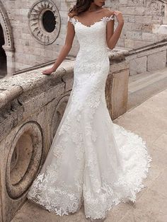 a woman in a white wedding dress standing on a stone wall with her back to the camera