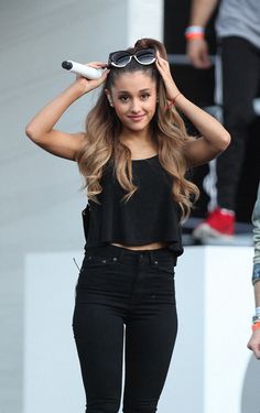 a woman in black pants and crop top holding her hair up to her head with one hand