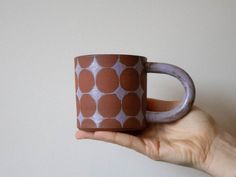 a hand holding a brown and white coffee cup with circles on it's side