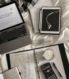 two laptops and a calculator are on a bed with notebooks, books, and papers