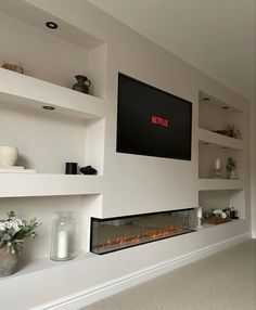 a television mounted on the wall above a fireplace with candles and flowers in vases