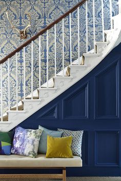 a white staircase with blue walls and colorful pillows on the bench in front of it