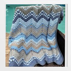 a crocheted blanket sitting on top of a wooden bench next to a swimming pool