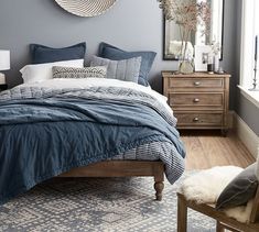 a bedroom with gray walls and blue bedding, white rugs and wooden furniture