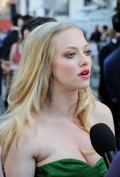 a woman with long blonde hair wearing a green strapless dress and holding a microphone