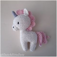 a crocheted stuffed unicorn laying on top of a white table next to a wall