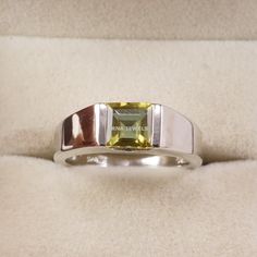 a white gold ring with a green tourmaline in the center on a velvet surface