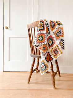 a wooden chair with a crocheted blanket on it's back in front of a white door