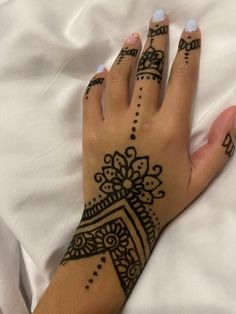 a woman's hand with henna tattoos on it and white sheets in the background