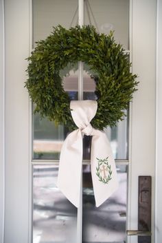 a wreath on the front door with a white bow hanging from it's side