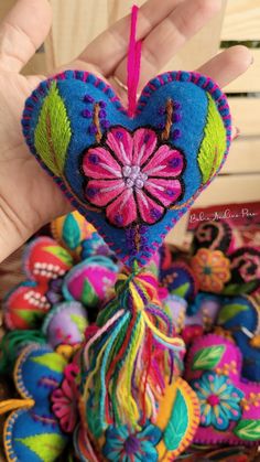 a hand holding a heart shaped ornament in the shape of a flower with tassels