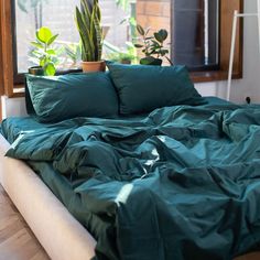 an unmade bed in front of a window with potted plants on the windowsill