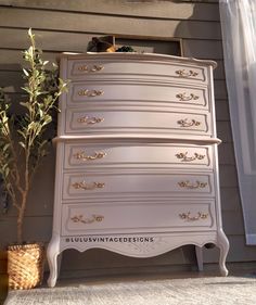 an old dresser is painted white with gold trim and drawers on the bottom, next to a potted plant