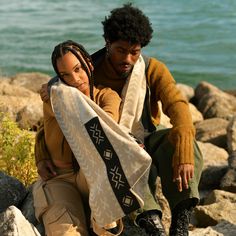 a man and woman sitting on rocks by the water with their arms around each other