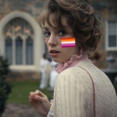 a woman with a rainbow strip on her face in front of a building and people