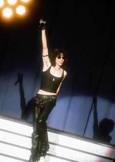 a woman with her arms up in the air while standing on stage at a concert