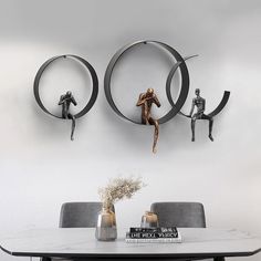 a dining room table with chairs and two metal sculptures on the wall above it,