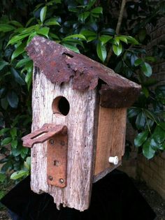 a bird house made out of wood and rusty metal parts, sitting in front of a bush