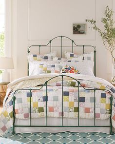 a bed with white sheets and colorful patchwork quilts on it, next to a potted plant