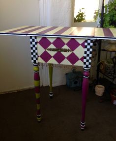 a table that has been painted with different colors and patterns on it, sitting next to a potted plant