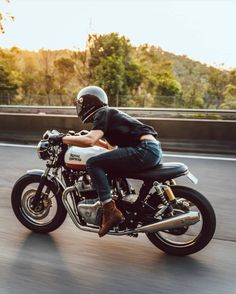 a man riding on the back of a motorcycle down a road with trees in the background