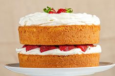 two cakes with strawberries on top are sitting on a cake plate, one is frosted and the other is covered in icing