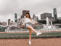 a woman is posing in front of a fountain with her legs spread out and one leg up