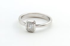 a white gold engagement ring with an emerald cut diamond in the center, on a plain surface