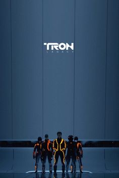 three men in yellow and black suits standing next to a wall with the word tron on it