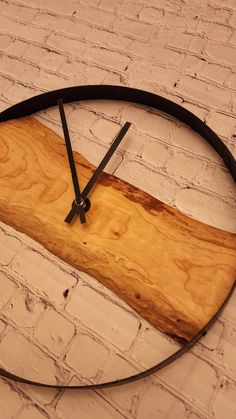 a clock made out of wood and metal on a white brick wall with black hands