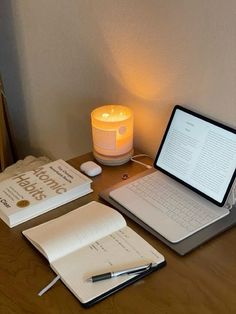 an open notebook sitting on top of a wooden desk next to a laptop computer and a lit candle