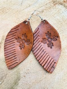 two brown leather earrings with flowers on them sitting on top of a stone surface next to a pair of silver earwires