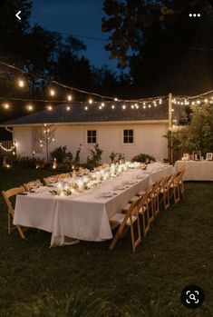 a long table is set up outside with candles and lights strung over it for an outdoor dinner