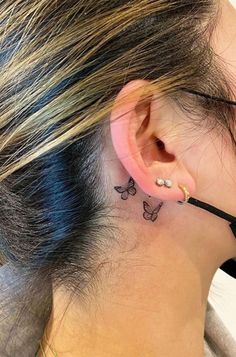 a woman with a small butterfly tattoo on her left behind the ear is looking down