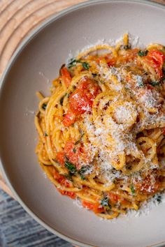 a white plate topped with pasta covered in parmesan cheese and tomato sauce on top of a wooden table